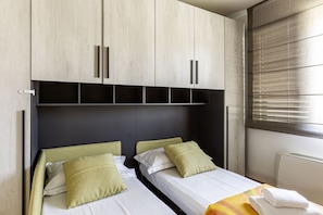A bedroom with two beds, a wardrobe, and a window with blinds.