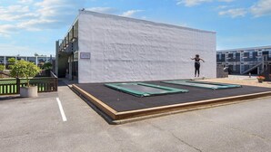 A trampoline area with a white wall backdrop, a small outdoor seating area, and a building with a balcony in the background. - 6 Person Holiday Park Home in Glesborg (Glesborg)