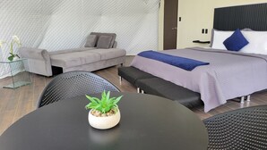 Ein modernes Hotelzimmer mit Bett, Sofa, Esstisch und einer Zimmerpflanze.