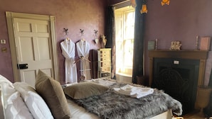 A bedroom with a bed, pillows, a fur throw, a dresser, a mirror, and a fireplace.