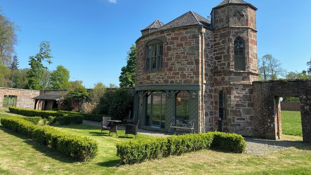 A stone building with a tower, a covered patio, and a well-maintained garden.