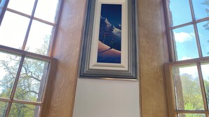 A room with two large arched windows, a framed painting of a landscape, and a ceiling with a mural of cherubs and a vine.