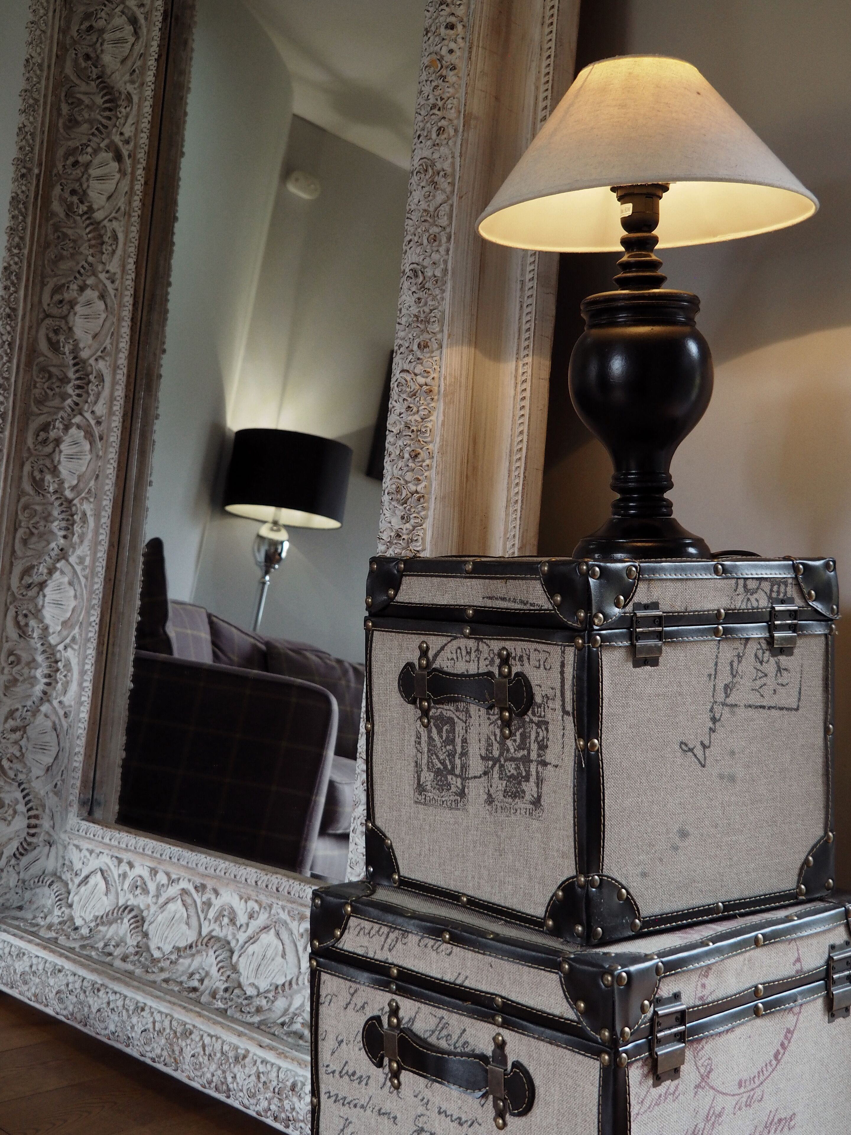 A lamp on a table with a mirror and two vintage suitcases stacked on a dresser.