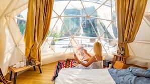 A cozy tent with a large window, a bed, and a table with a newspaper. - Phuwin Homestay Monjam (Mae Rim)
