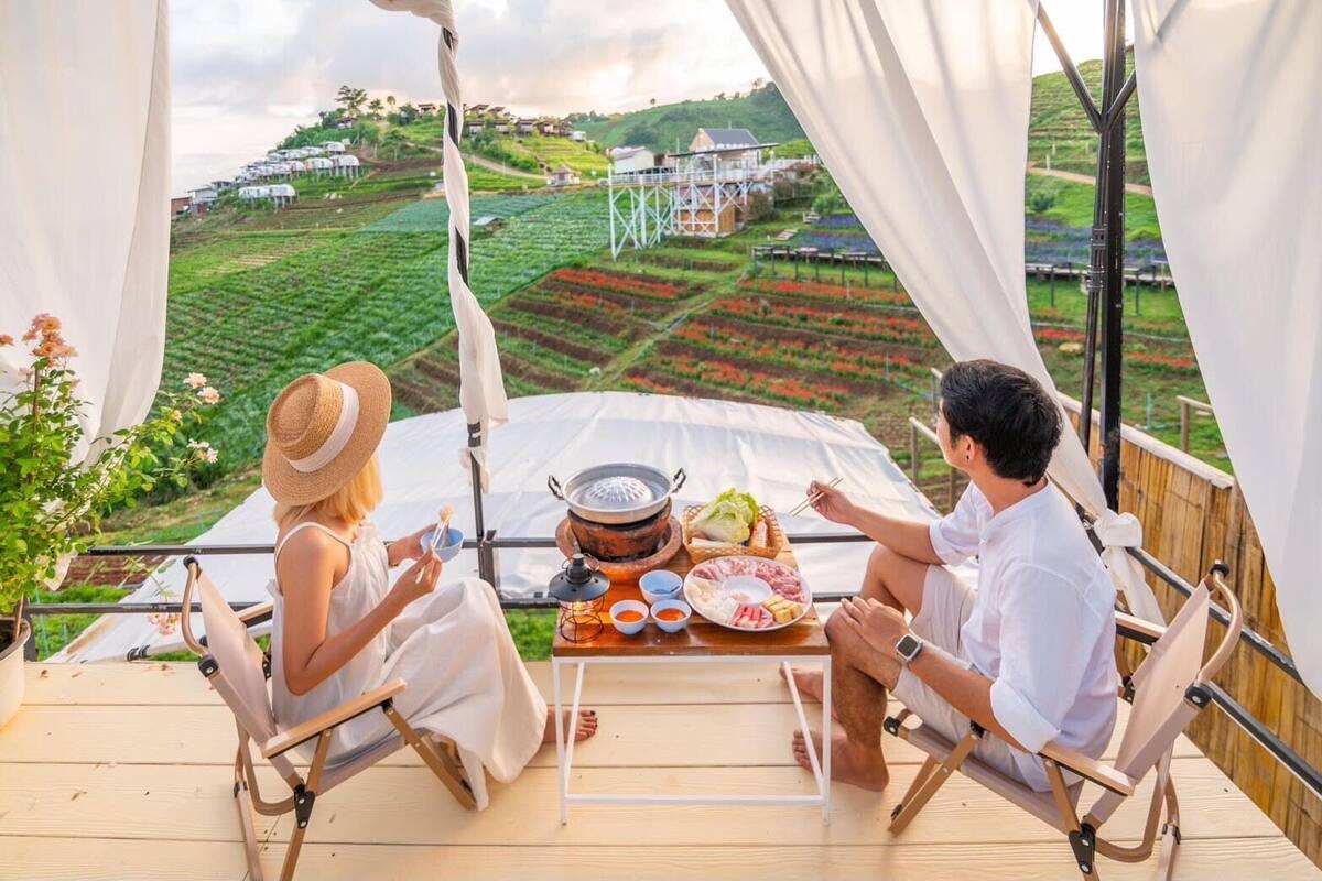 Two people dining on a wooden deck with a table set for a meal, overlooking a vineyard.