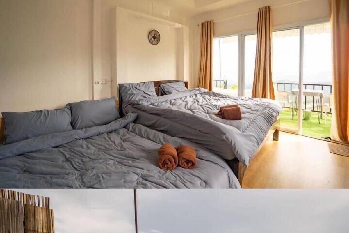 A bedroom with a large bed, a clock on the wall, and a view of a balcony with a view of the mountains.