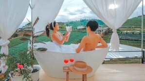 A couple in a bathtub with a scenic view of green fields and a house in the background. - Phuwin Homestay Monjam (Mae Rim)