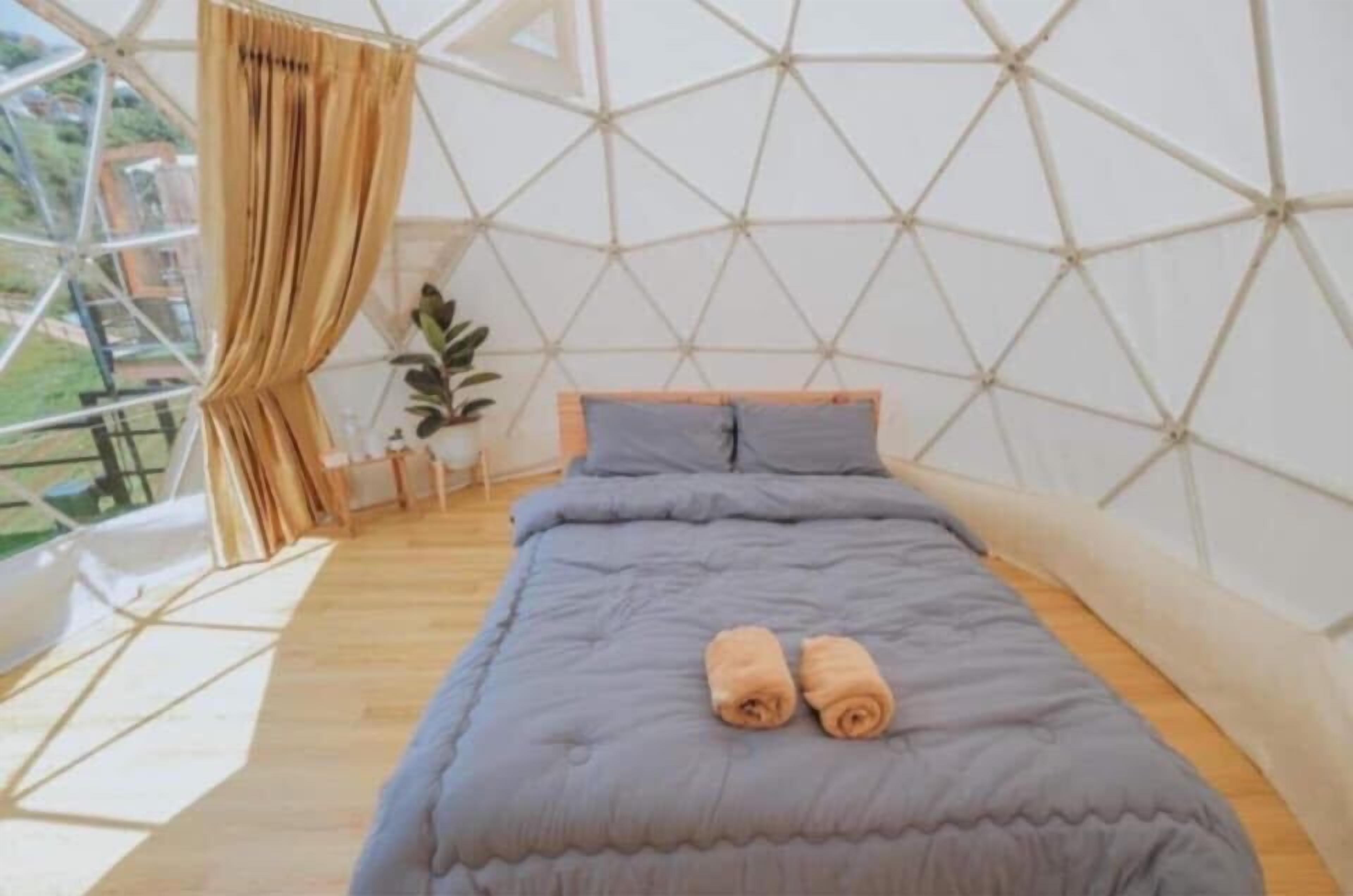 Ein Zimmer mit einem geometrischen Deckenmuster, einem Bett mit grauer Bettdecke und zwei gerollten Handtüchern auf dem Bett.