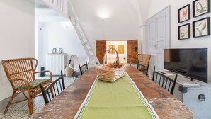 A dining area with a long wooden table, wicker chairs, a green runner, and a television on a stand.