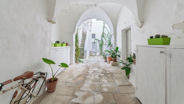 A narrow stone pathway flanked by white walls and arches, leading to a staircase.