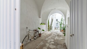 A narrow, arched corridor with a bicycle and potted plants, leading to a staircase.