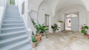 A white-walled corridor with a staircase, potted plants, and a bicycle.