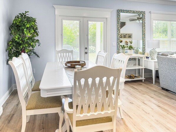 A dining area with a white table and chairs, a potted plant, and a view through a door.