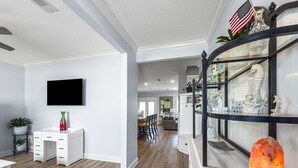 A spacious living room with a flat-screen TV, a white desk, and a glass display cabinet with decorative items. - 5 Bedroom | Sleeps 19 | Eagles Dune | Patio | Santa Rosa Beach (Santa Rosa Beach)