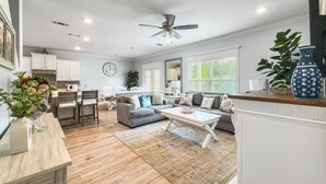 A spacious living room with a sofa, coffee table, and a dining area with chairs and a kitchen in the background. - 5 Bedroom | Sleeps 19 | Eagles Dune | Patio | Santa Rosa Beach (Santa Rosa Beach)