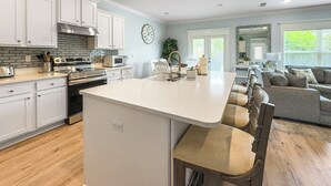 A modern kitchen with white cabinetry, a central island, and a seating area with a sofa and chairs. - 5 Bedroom | Sleeps 19 | Eagles Dune | Patio | Santa Rosa Beach (Santa Rosa Beach)