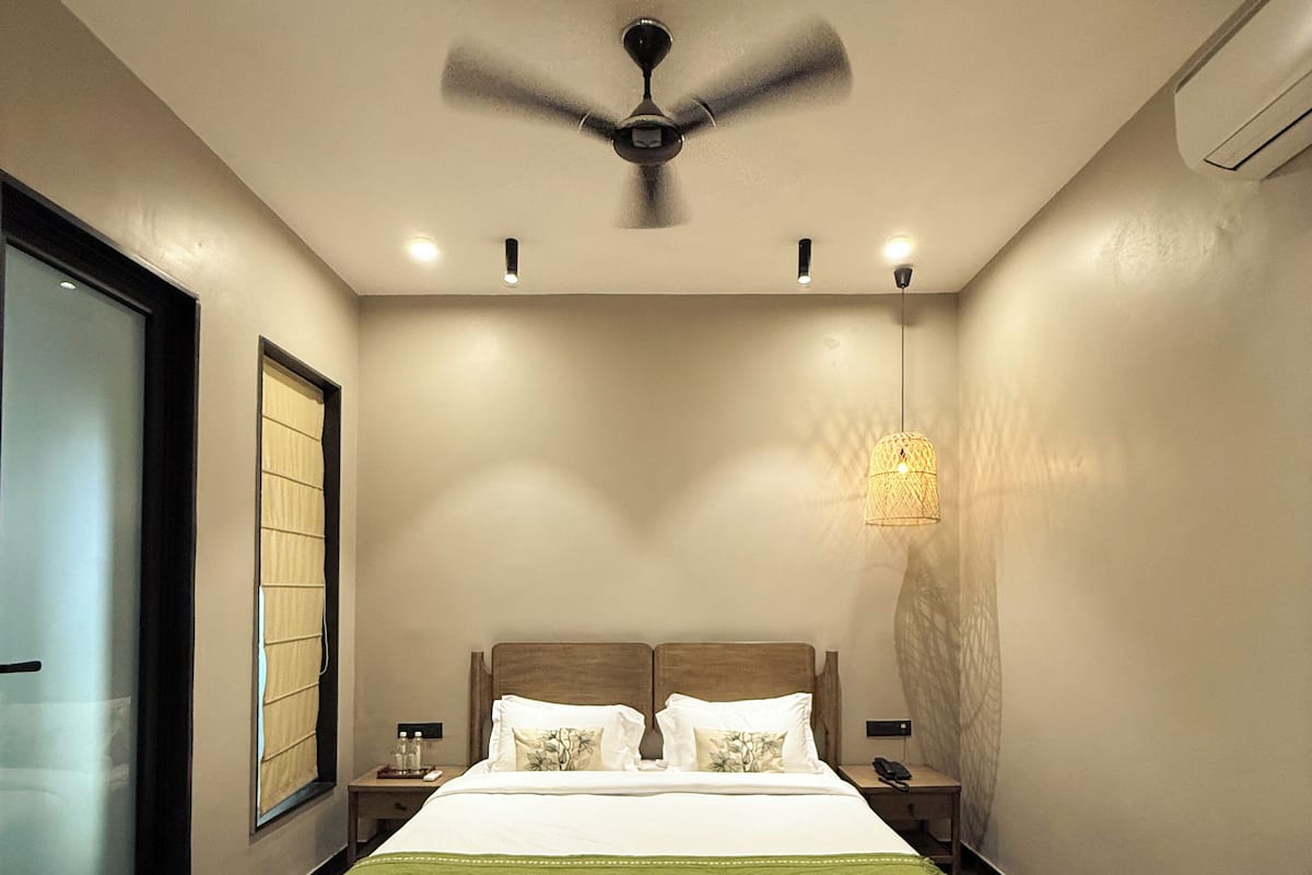 A modern hotel room with a large bed, a ceiling fan, a bedside table with a lamp, and a view of the outside.