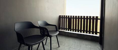 A balcony with two black chairs, a wooden ceiling, and a view of the sky.