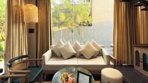 A modern living room with a sofa, chairs, a table with a basket of snacks, and a ceiling fan. - THE BALI HOUSE (Bhopal)