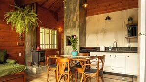 Ein gemütliches Blockhäuschen mit Essbereich, Holzwänden, einem Kamin aus Stein und einer Küche mit weißen Schränken.