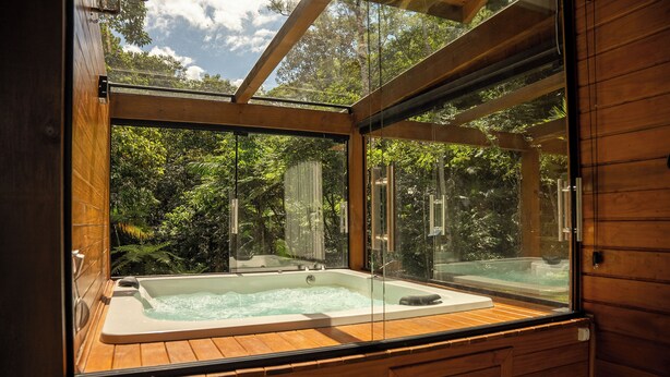 Eine hölzerne Badewanne mit Glastrennwand, umgeben von Holzwänden und einem Glasfenster.