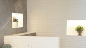 A modern bathroom with a white sink, a small potted plant, and a trash can.