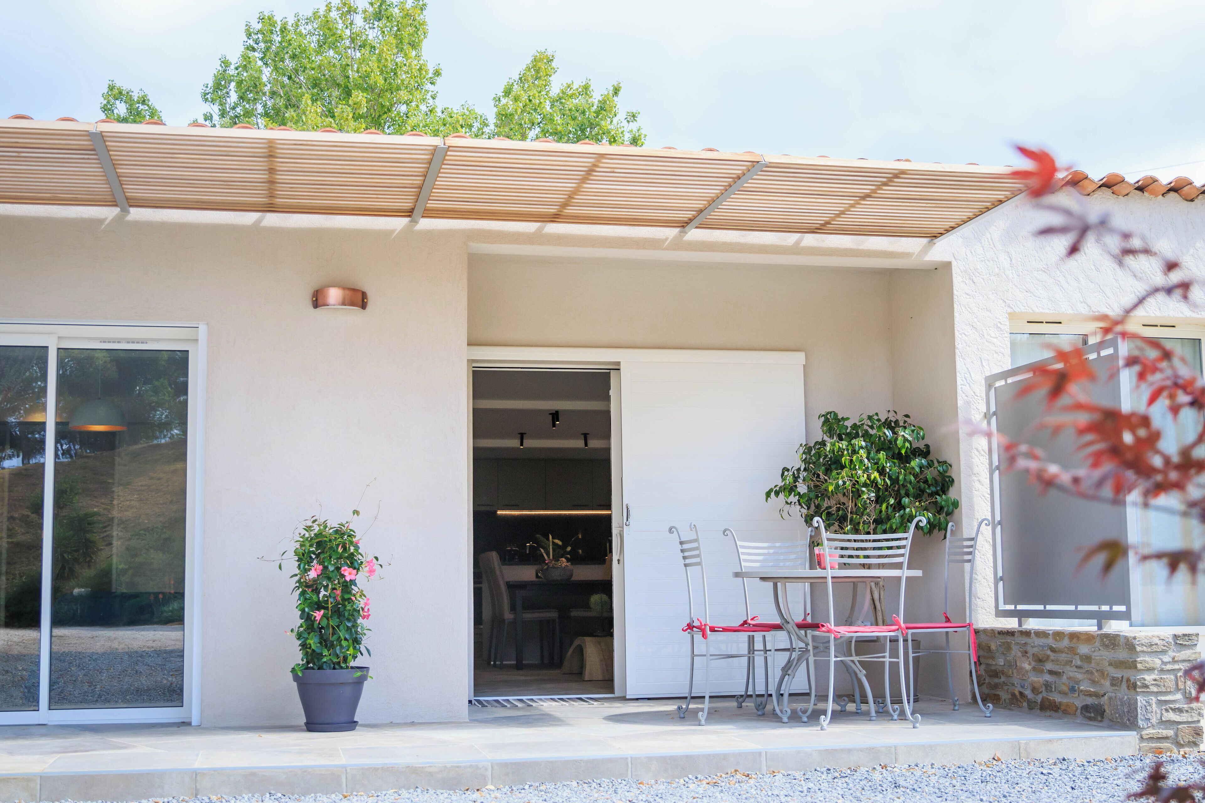 A modern house with a patio area featuring a table and chairs, a potted plant, and a sliding glass door leading to an interior space.