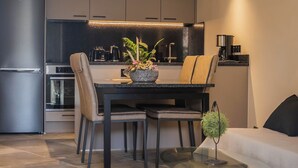 A modern kitchen with dark cabinetry, a built-in oven, and a dining area with a glass table and chairs.