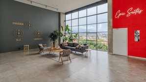 Amplia sala de estar con un ventanal grande, una pared gris con nombres de ciudades, una pared de acento roja y una disposición de mobiliario moderno.