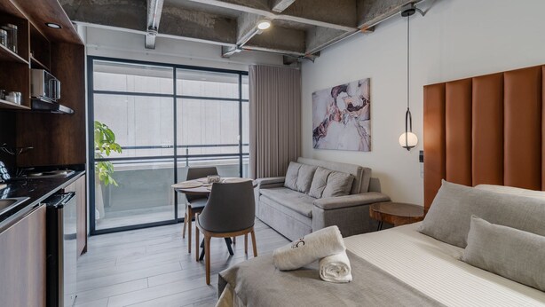 Ein modernes Hotelzimmer mit großem Fenster, einer Couch, einem Bett und einem Essbereich.