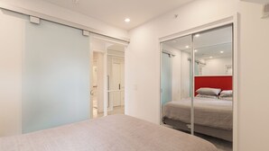A bedroom with a bed, a sliding door, a mirror, and a red accent wall. - Luxury Downtown Suite w/ Balcony Views, Air Conditioning + Free Parking (Calgary)