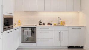A modern kitchen with white cabinets, a built-in oven, and a stainless steel range hood. - Luxury Downtown Suite w/ Balcony Views, Air Conditioning + Free Parking (Calgary)