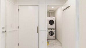 A laundry room with stacked washing machines, a closed door, and a tiled floor. - Luxury Downtown Suite w/ Balcony Views, Air Conditioning + Free Parking (Calgary)