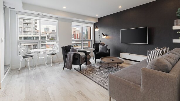 A modern living room with a large window, a flat-screen TV, and a sofa. - Luxury Downtown Suite w/ Balcony Views, Air Conditioning + Free Parking (Calgary)