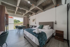 Een moderne hotelkamer met een groot bed, een zithoek met stoelen en uitzicht op het omliggende landschap.