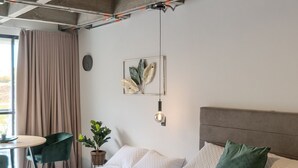 Ein modernes Schlafzimmer mit einem großen Bett, einem Nachttisch, einem Sessel und einem Fenster mit Vorhängen.