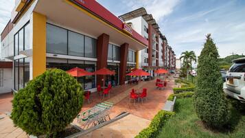A hotel with outdoor seating, red umbrellas, and a tiled patio.