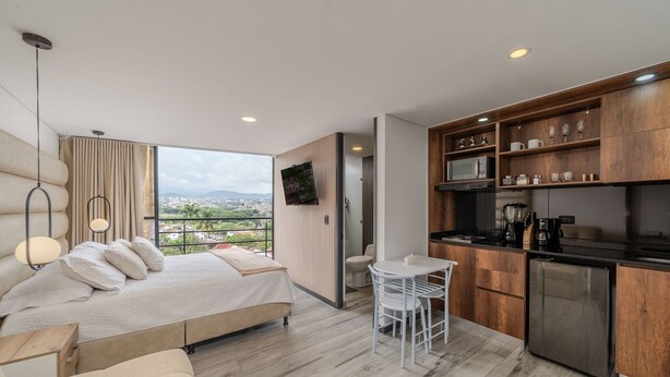 Una habitación de hotel moderna con una cama grande, una pequeña zona de cocina y un balcón con vistas a la ciudad.