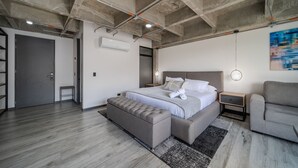 Un dormitorio moderno con una cama grande, un banco, una mesita de noche y un sofá gris.