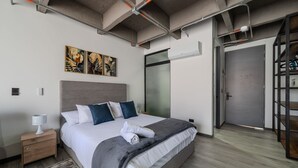 A modern hotel room with a large bed, a nightstand, a wall-mounted air conditioner, and a door leading to a hallway. - |Ahead| Captivating Loft with Parking and AC (Pereira)