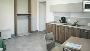 Una cocina moderna con microondas, cafetera y un pequeño comedor con una silla.