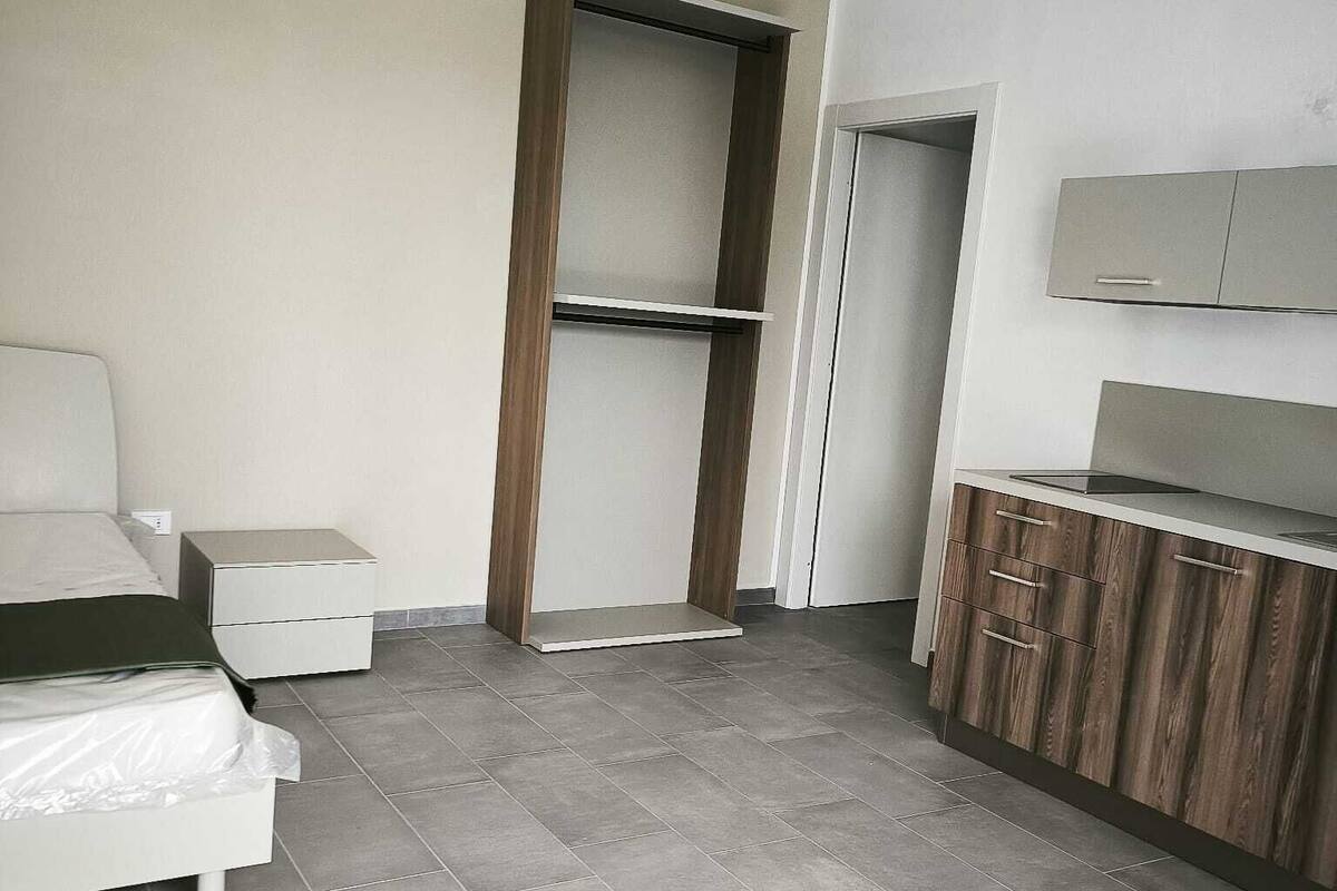 A modern, minimalist bedroom with a bed, bedside table, wardrobe, and a built-in shelf unit.