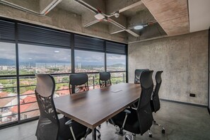 Ein Konferenzraum mit großem Tisch und vier Stühlen, großen Fenstern mit Stadtblick und einer Betondecke mit freiliegenden Balken und Leuchten.