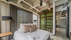 A modern bedroom with a large bed, a bench, a hanging light, and a green wall with shelves.