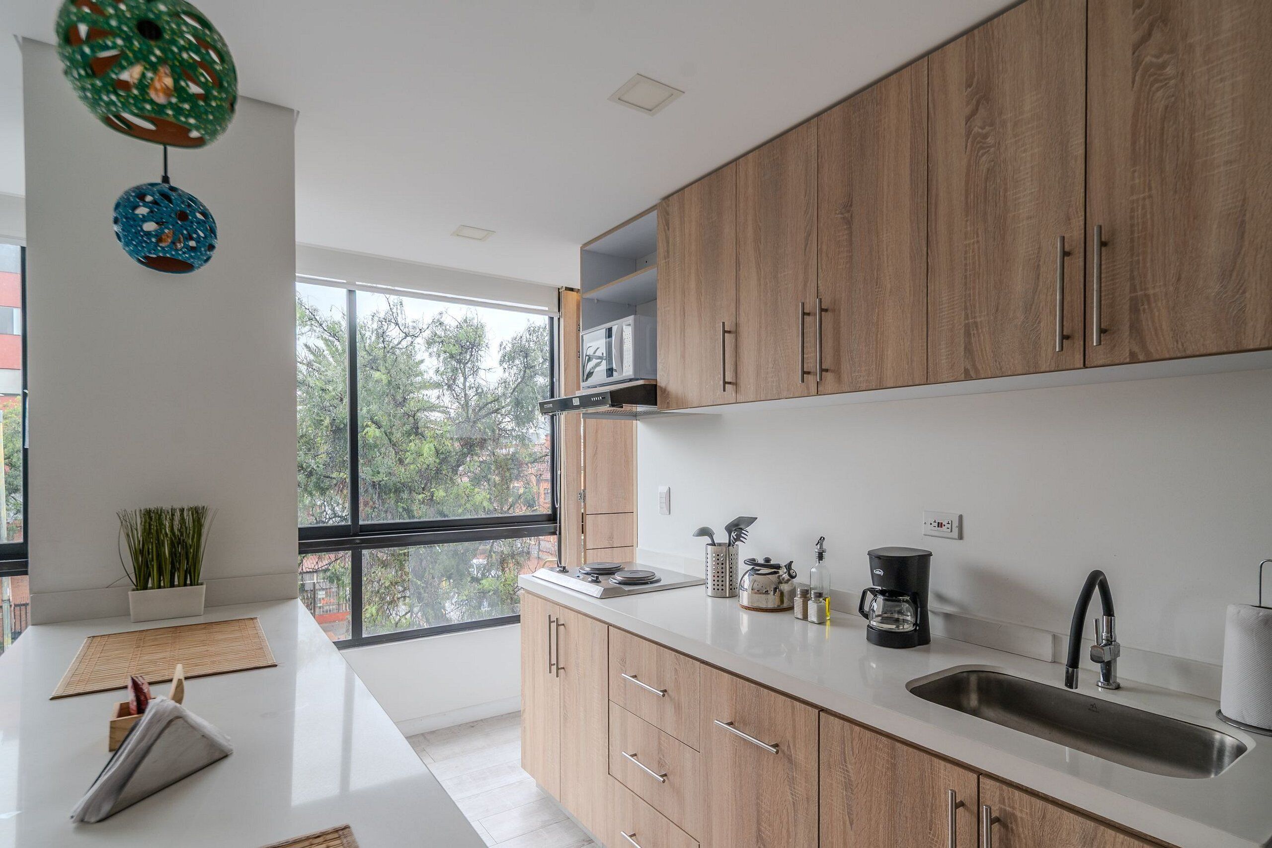 Una cocina moderna con armarios de madera, una encimera blanca y un amplio ventanal con vistas a árboles.