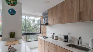 Una cocina moderna con armarios de madera, una encimera blanca y un amplio ventanal con vistas a árboles.