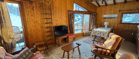 A cozy wooden interior with a TV, sofa, and dining area.