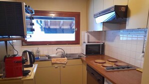 A compact kitchen with a window, a microwave, a Bosch dishwasher, and a red coffee maker.