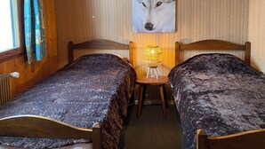 A room with two wooden beds, a wall-mounted lamp, and a large painting of a wolf's face.
