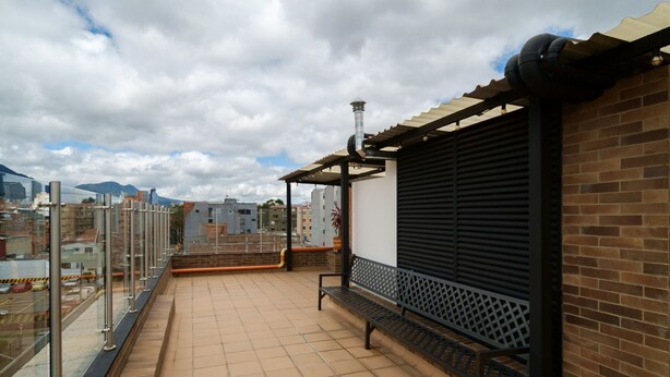 Un balcon doté d’un sol carrelé, d’un banc en métal et offrant une vue sur le paysage urbain.